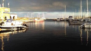 Ein Yachthafen mit mehreren vertäuten Booten, einem Gebäude mit Bögen und einem bewölkten Himmel.