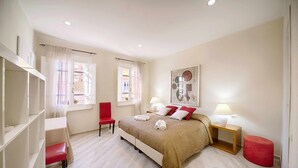 Ein Schlafzimmer mit Bett, einem Sessel, einem Nachttisch mit Lampe und einem roten Hocker.