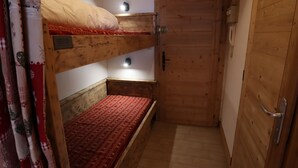 A small, wooden room with a bunk bed, a single bed, and a door. - Central Studio at Foot of Les Gets Pistes – Refurbished, Scenic Views, Sleeps 4 (Les Gets)