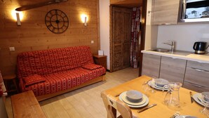 A cozy room with a wooden sofa, a dining table set with plates and glasses, and a kitchen area with a microwave. - Central Studio at Foot of Les Gets Pistes – Refurbished, Scenic Views, Sleeps 4 (Les Gets)