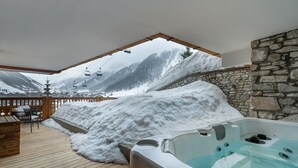 Eine Holzterrasse mit Whirlpool und Schneematsch, mit Blick auf einen Berg und eine Seilbahn.