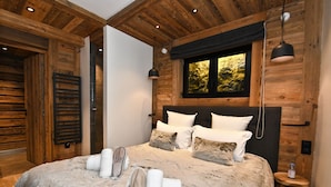 Ein Schlafzimmer mit einem großen Bett, Holzwänden, einem Fenster mit Blick und einem kleinen Hocker mit einer Flasche.