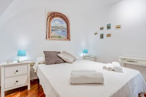 Une chambre d’hôtel comprenant un lit, deux tables de chevet avec des lampes, une table d’appoint, un tableau accroché au mur et un petit bureau avec une chaise.