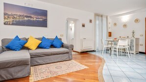 A living room with a sofa, a dining table with chairs, a view of a cityscape, and a patterned rug.