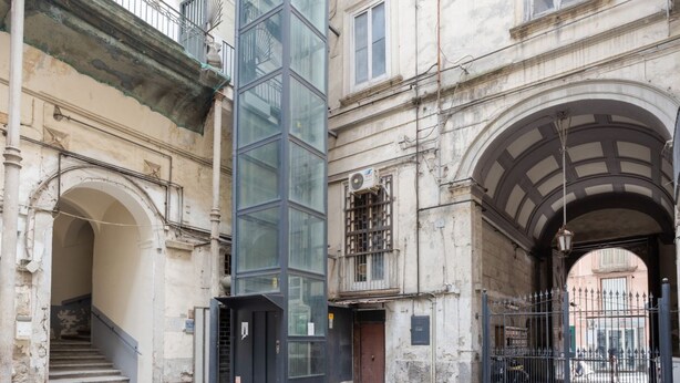 A historic building with a central glass tower, an arched entrance, and a staircase leading to an upper level.