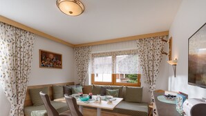 A cozy room with a wooden bench, a table, and chairs. There is a window with curtains, a painting on the wall, and a lamp. - Apartment Waltraud (Uderns)