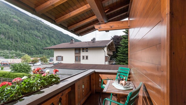 A wooden balcony with a table and chairs, overlooking a mountain and a small house. - Apartment Waltraud (Uderns)