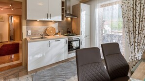 A modern kitchen with white cabinets, a stove, and a sink. There are two chairs and a small table. - Apartment Waltraud (Uderns)