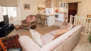 Un espace de vie compact comprenant un canapé, une petite table basse, un téléviseur et un coin cuisine avec une table à manger et des tabourets de bar.