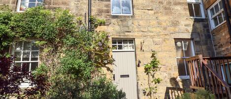 A stone building with multiple windows, a door, and a small garden area with potted plants.