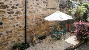 Un mur de pierres, un parasol blanc et une table avec des chaises dans un espace aménagé en jardin.