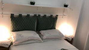 En pænt redt seng med grønne mønstrede puder, et hvidt dynebetræk og en sengegavl med to små sorte kurve.