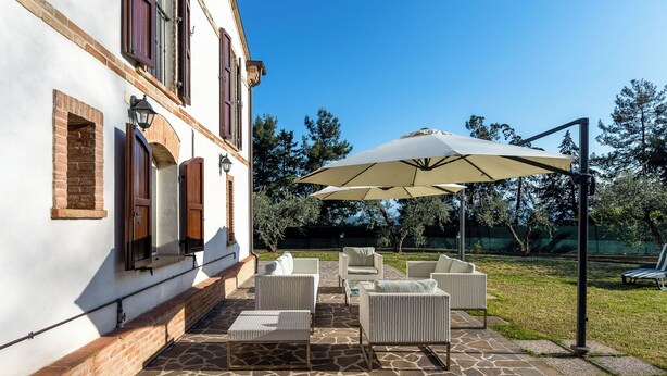 A patio with wicker furniture and a large umbrella, set against a white building with brick accents.