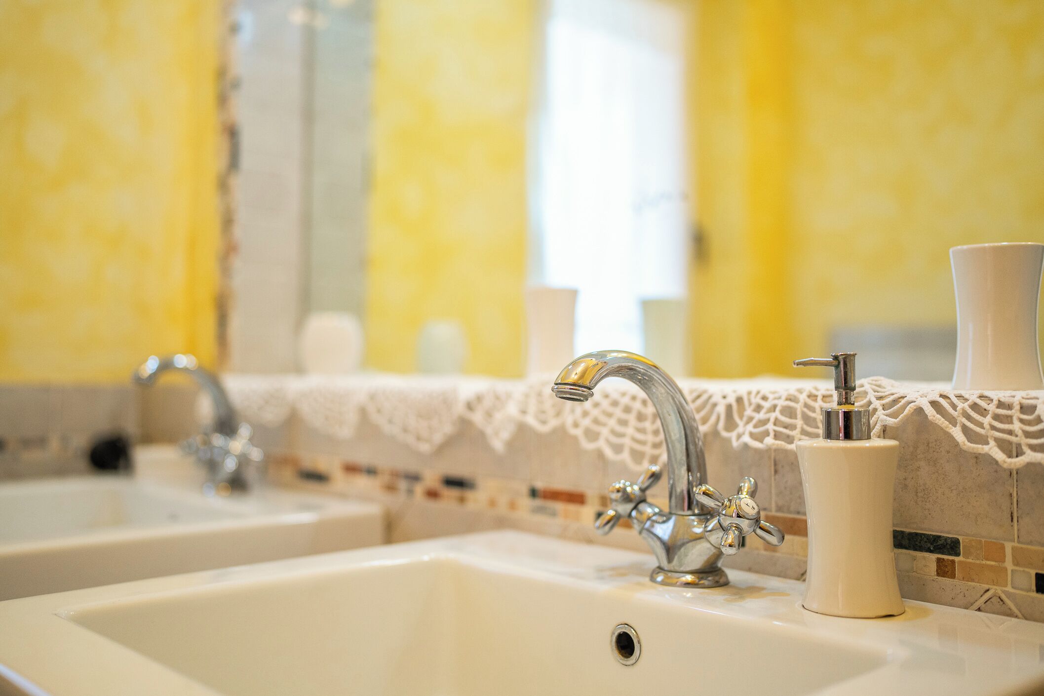 A bathroom with two sinks, a mirror, and a lace-trimmed counter.