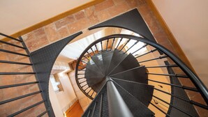 A spiral staircase with a black metal handrail and black steps, leading to a landing area with a brick wall and a wooden floor.