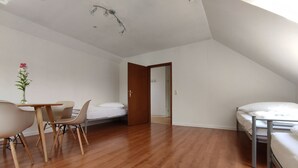 A small, bright room with a wooden floor, a bed, a desk with chairs, and a door leading to another room. - Ferienwohnung Family Basic in Kiel (Kiel)