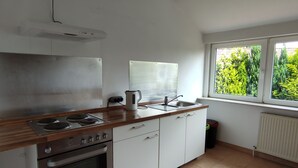 A kitchen with a stove, oven, sink, and window overlooking greenery. - Ferienwohnung Family Basic in Kiel (Kiel)