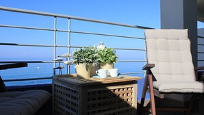 A balcony with a view of the sea, a cushioned chair, a small table with potted plants and cups, and a wooden crate. - Appartamento Sulla Spiaggia (Villafranca Tirrena)