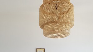 A white dining table with four chairs, a woven pendant light, and a framed picture on the wall. - Appartamento Sulla Spiaggia (Villafranca Tirrena)