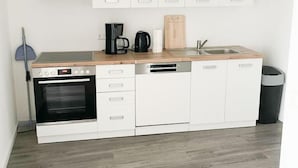 Una cocina moderna con armarios blancos, horno empotrado, lavavajillas y cafetera.