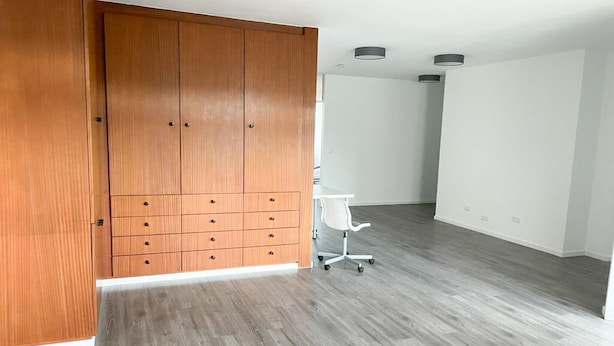 Una habitación con un armario de madera, una silla de oficina blanca y un suelo gris.