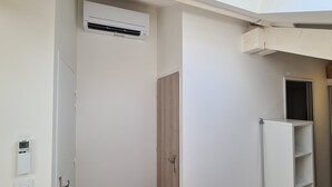 Quarto com ar condicionado branco, porta de madeira e estante branca.