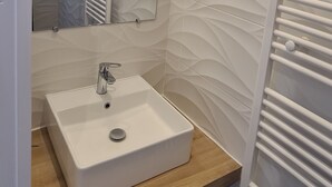 Uma casa de banho moderna com uma pia branca, um espelho e um porta-toalhas.