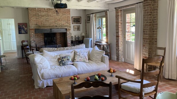 A cozy living room with a white sofa, a wooden table with fruit, and a brick fireplace.
