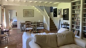 A cozy living room with a sofa, a dining area with chairs, a staircase, and a bookshelf filled with books.