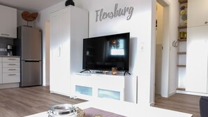A modern kitchen with white cabinets, a stainless steel refrigerator, and a flat-screen TV mounted above a white countertop. - fewo1846 - MuschelNest (App. (Harrislee)
