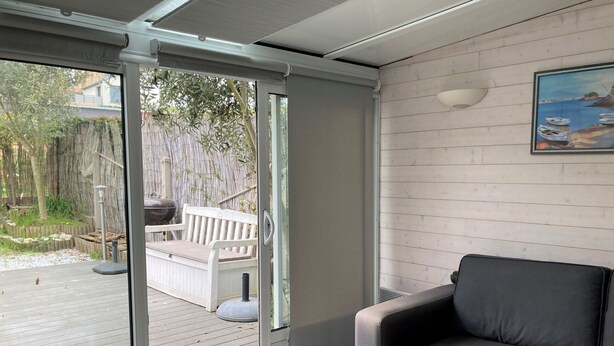 Un salon moderne avec un canapé gris, une porte-fenêtre coulissante donnant sur une terrasse en bois et un tableau accroché au mur.