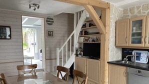 Un coin repas avec une table et des chaises en bois, un téléviseur et un espace cuisine doté de meubles et d’un évier en bois.