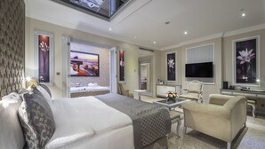 Une chambre d’hôtel spacieuse, dotée d’un grand lit, d’un coin salon avec une table basse, d’une télévision et d’une salle de bain avec baignoire et douche.