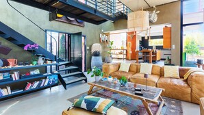 A spacious living area with a leather sofa, coffee table, and bookshelves. A staircase leads to an upper level. - VILLA SUNSET VI4236 By Riviera Holiday Homes (Niza)