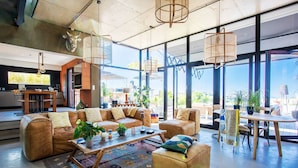 A spacious living area with leather sofas, a coffee table, and a dining table with chairs. Large windows provide a view of the outdoors. - VILLA SUNSET VI4236 By Riviera Holiday Homes (Niza)