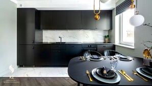 Une cuisine moderne avec des meubles de couleur sombre, un plan de travail en marbre et un coin repas aménagé pour quatre personnes, avec une table noire et des couverts dorés.