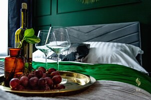 Una cama con una colcha verde, una botella de vino, una copa de vino y un plato de uvas sobre una bandeja.