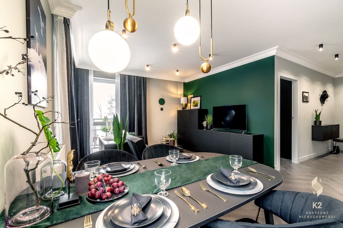 Un comedor moderno con una pared de acento verde oscuro, una mesa redonda preparada para cuatro personas y un televisor montado en la pared.