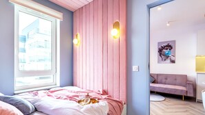 Une chambre à coucher avec un lit, une fenêtre, une tête de lit rose et un canapé rose dans la pièce adjacente.