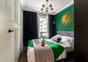 Ein Schlafzimmer mit Bett, einer grünen Akzentwand, einer Pendelleuchte und einem Fenster mit Vorhängen.