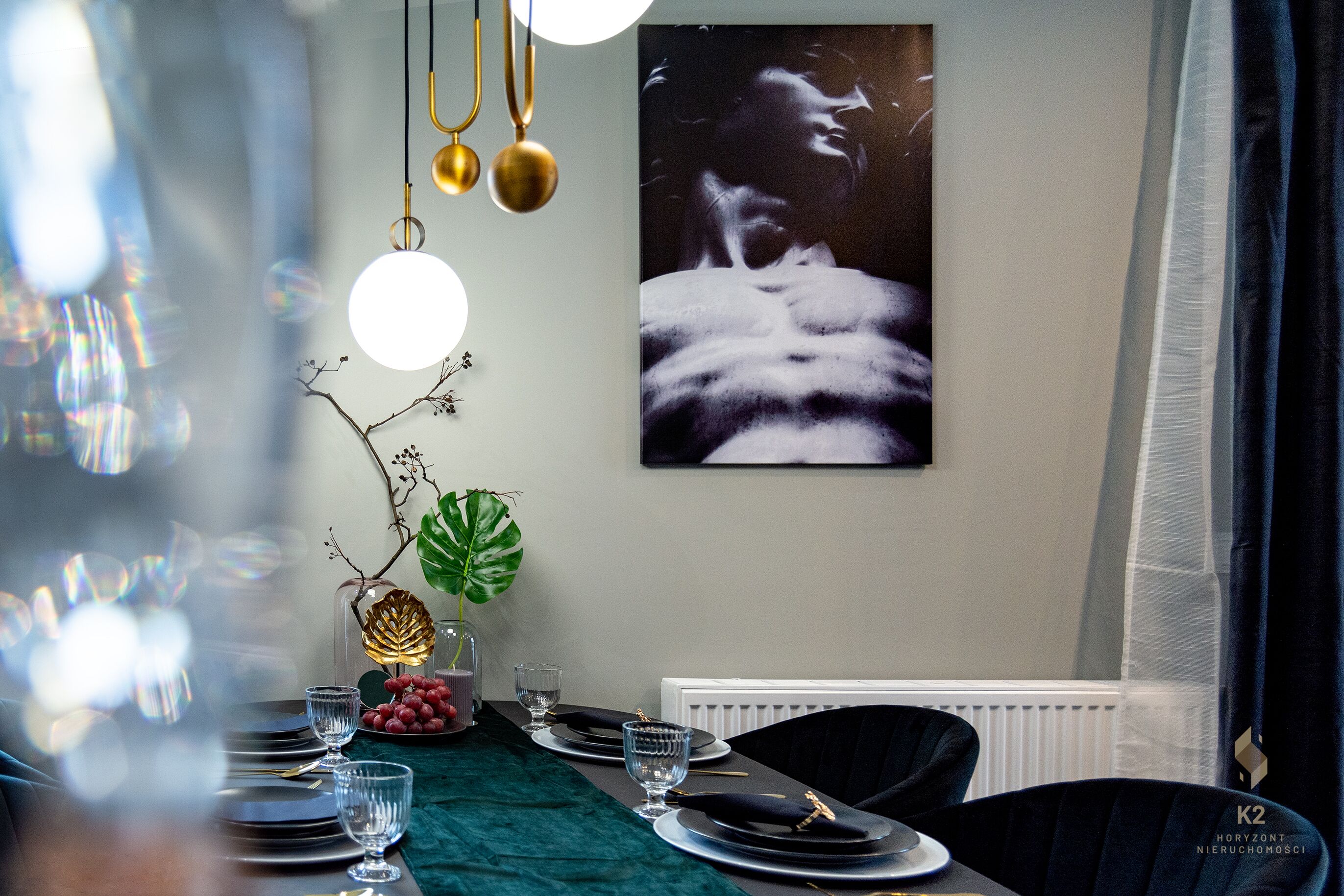 Een eetgedeelte met een tafel voor vier personen, een groot kunstwerk in een lijst aan de muur en een plant op de tafel.