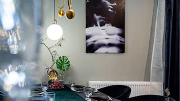 Een eetgedeelte met een tafel voor vier personen, een groot kunstwerk in een lijst aan de muur en een plant op de tafel.