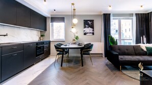 Une cuisine moderne avec des meubles de couleur sombre, un plan de travail en marbre et un coin repas comprenant une table ronde et des chaises.