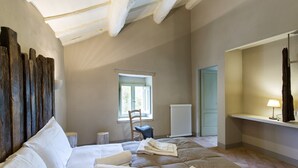 Un dormitorio con cama, una silla, un ventanal y un radiador.