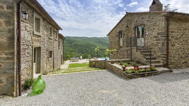 Un edificio de piedra con un patio de grava, una banca y vistas a la montaña.
