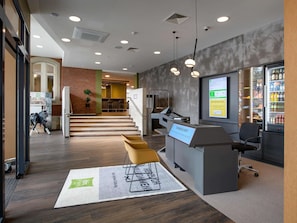 A modern reception area with a digital display, seating, a staircase, and a vending machine. - Ibis Styles Coburg (Coburg)