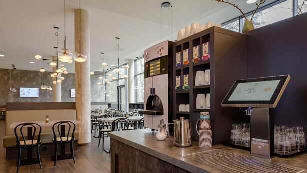 A modern cafe interior with a bar area, seating, and a coffee machine. - Ibis Styles Coburg (Coburg)