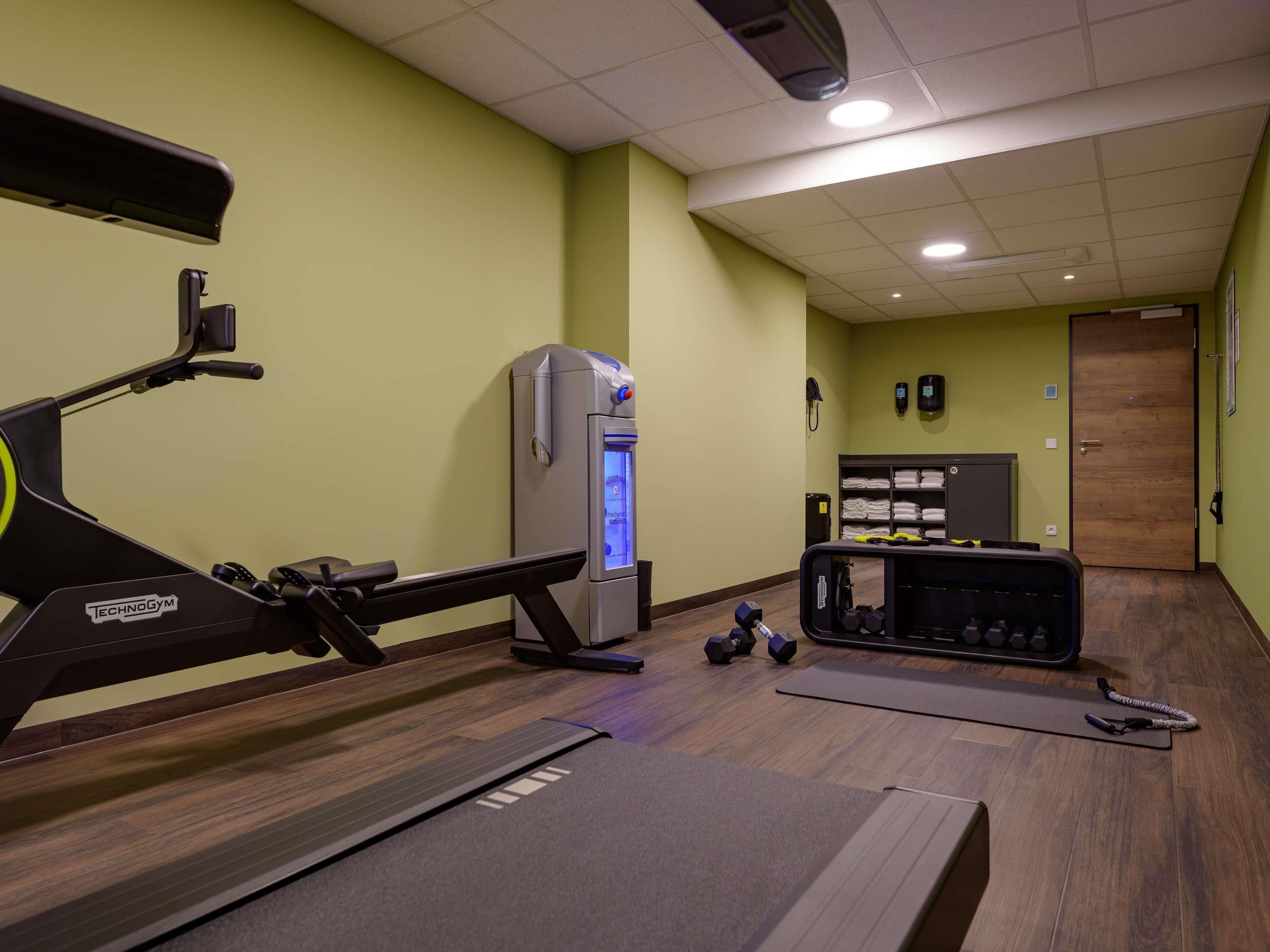 Un gimnasio con cinta de correr, pesas y dispensador de agua.