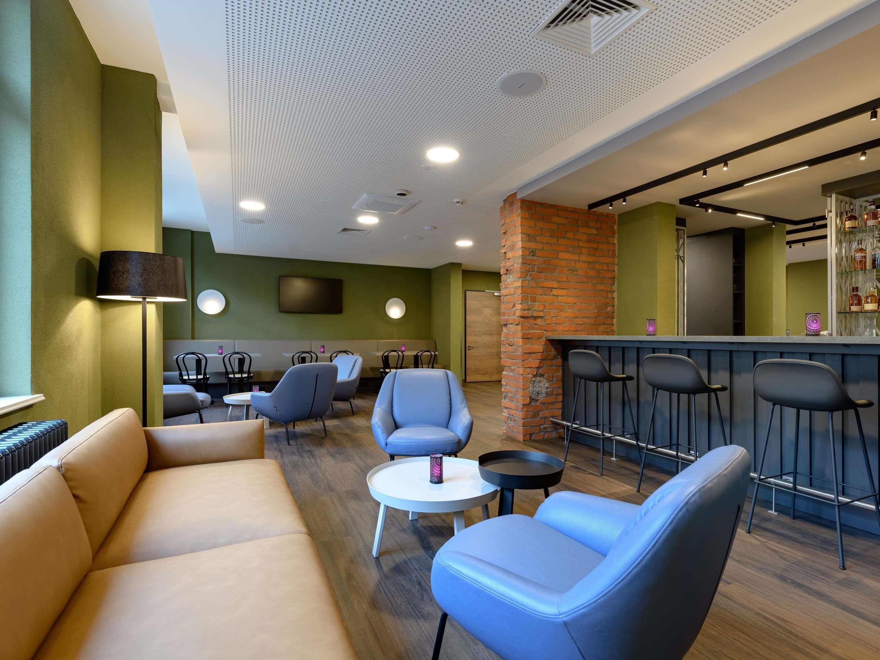 A modern lounge area with a sofa, armchairs, a small table, and a bar with stools.
