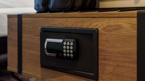 A hotel room with a wooden drawer containing a black electronic device, possibly a safe or lock system. - Ibis Styles Coburg (Coburg)
